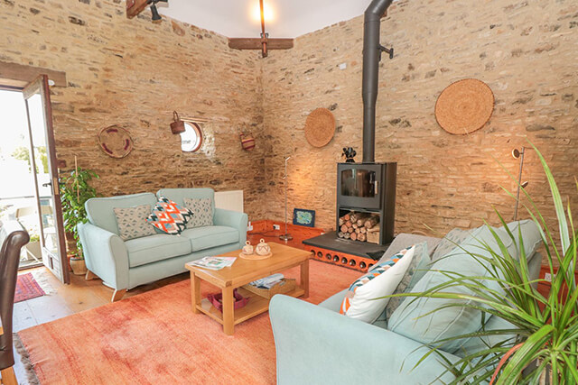 interior of a holiday cottage with woodburner, sofas, patio doors and indoor plants.