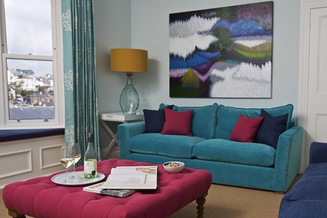 Living area with bright coloured sofas, wall art, lamp and view outside.