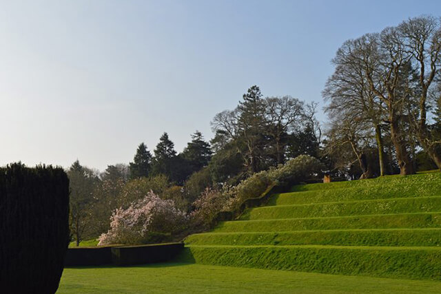 Dartington hall gardens - tiered lawns with trees and blue sky.