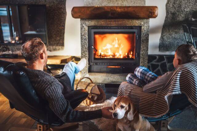 A father and son get warm by the fire with their dog.