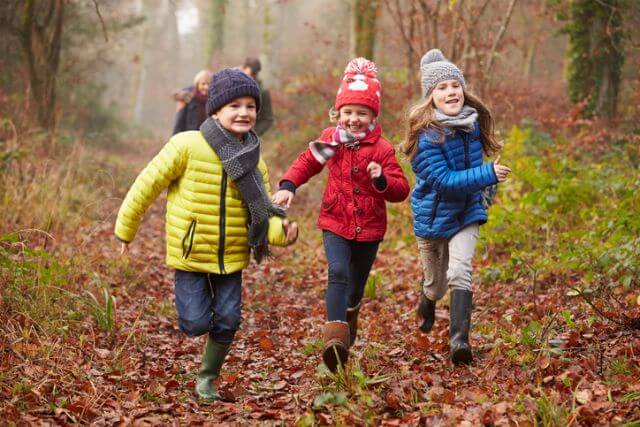 Three children running through a forest in winter.