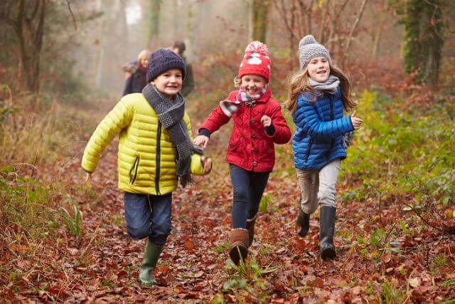 Three children running through a forest in winter.