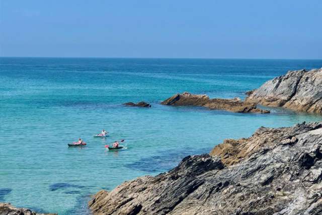 Three kayaks floating on the sea with cliffs in the foreground, on a sunny day